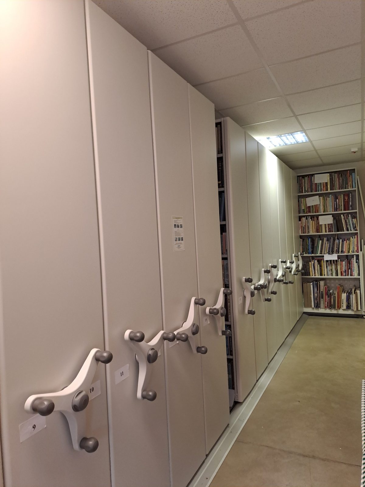 Mobile shelving units in the BEHT library, with the open reading area visible beyond.